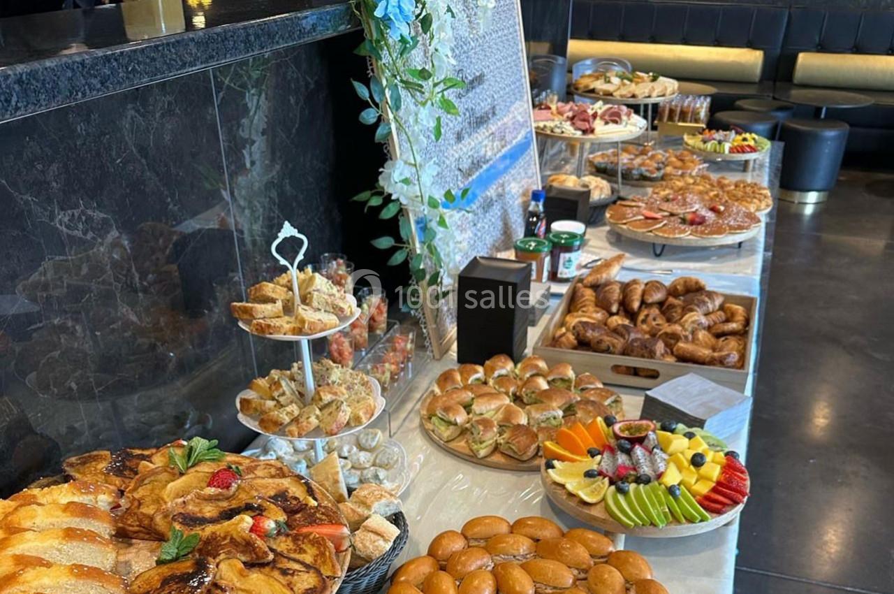 Buffet varié avec viennoiseries, fruits, sandwichs, et autres plats disposés sur une table dans un cadre élégant.