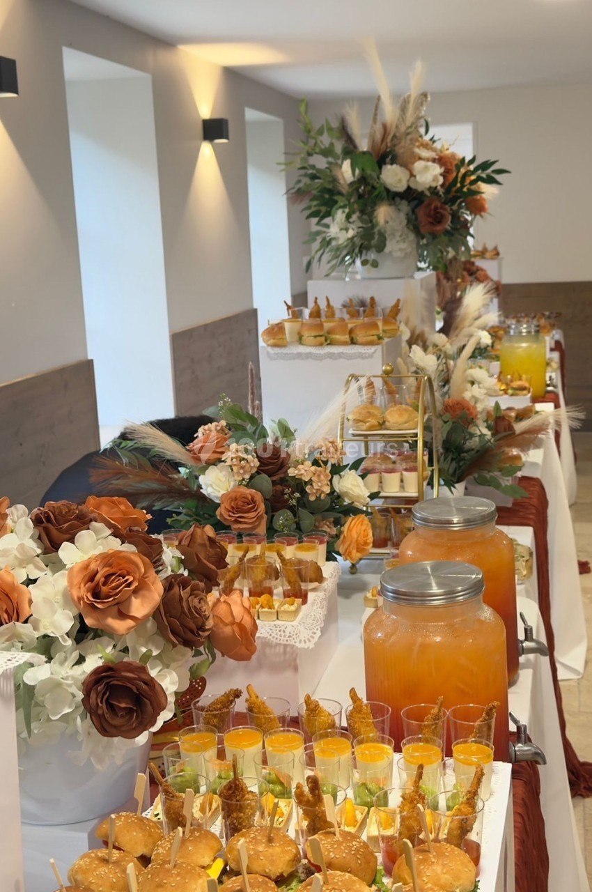 Table décorée avec des fleurs et des boissons, présentant un buffet de desserts et de verrines dans une ambiance élégante.