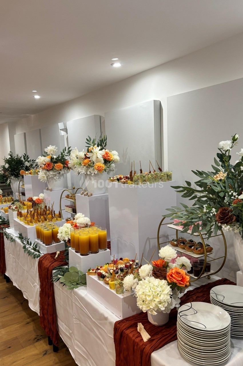 Buffet décoré avec des fleurs et des boissons, comprenant des desserts et des verrines sur une table élégante.