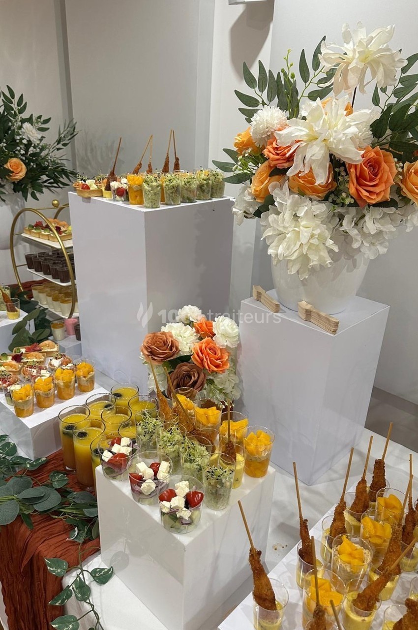 Buffet élégant avec verrines colorées, brochettes apéritives et décoration florale composée de roses et dahlias.