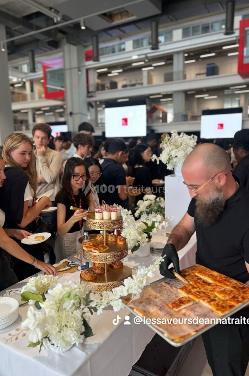 Un traiteur sert des plats lors d'un buffet élégant avec des invités autour d'une table décorée de fleurs blanches.