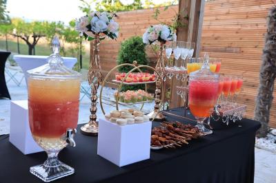 Table de buffet en extérieur avec boissons, verrines, macarons, brochettes et décorations florales élégantes.