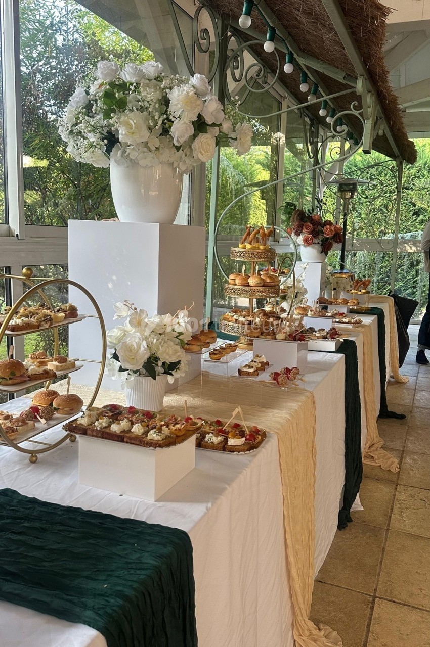 Table garnie de pâtisseries variées, présentées sur des présentoirs élégants, entourée de décorations florales.