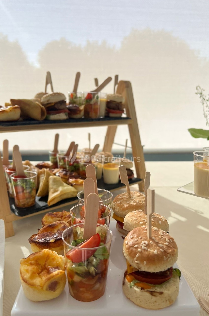 Plateau de bouchées salées variées, incluant mini-burgers, verrines et feuilletés, disposé sur une table lumineuse.