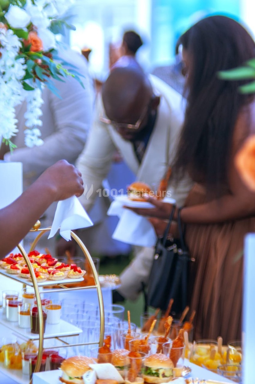Personnes se servant à un buffet avec des plats variés, dont des burgers, verrines et desserts, dans un cadre élégant.