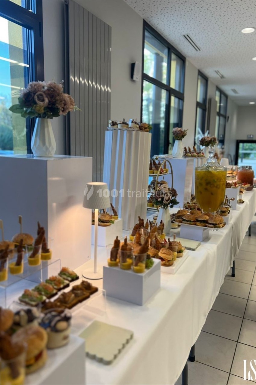 Buffet élégant avec des amuse-bouches variés, boissons et décorations florales dans une salle lumineuse.