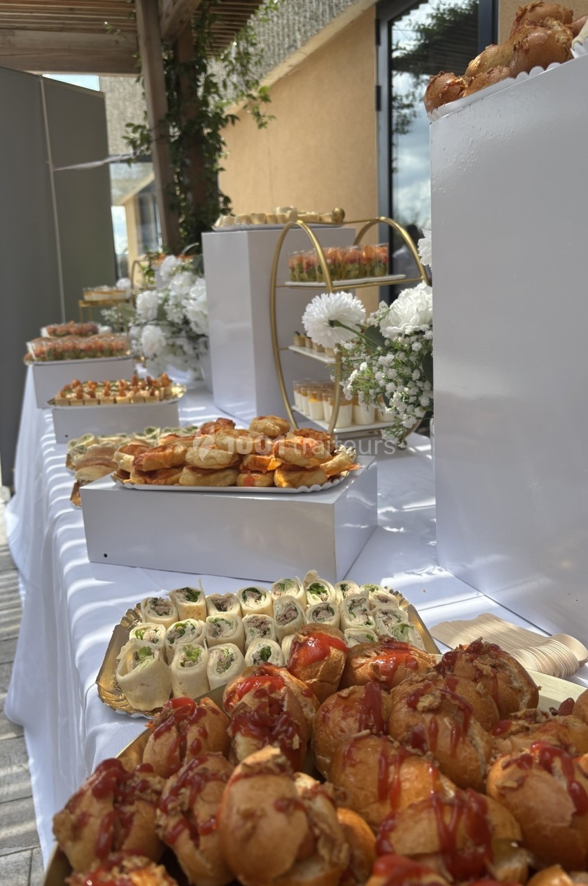 Buffet en extérieur avec des plateaux de bouchées salées et sucrées, décoré de fleurs blanches et d'éléments modernes.