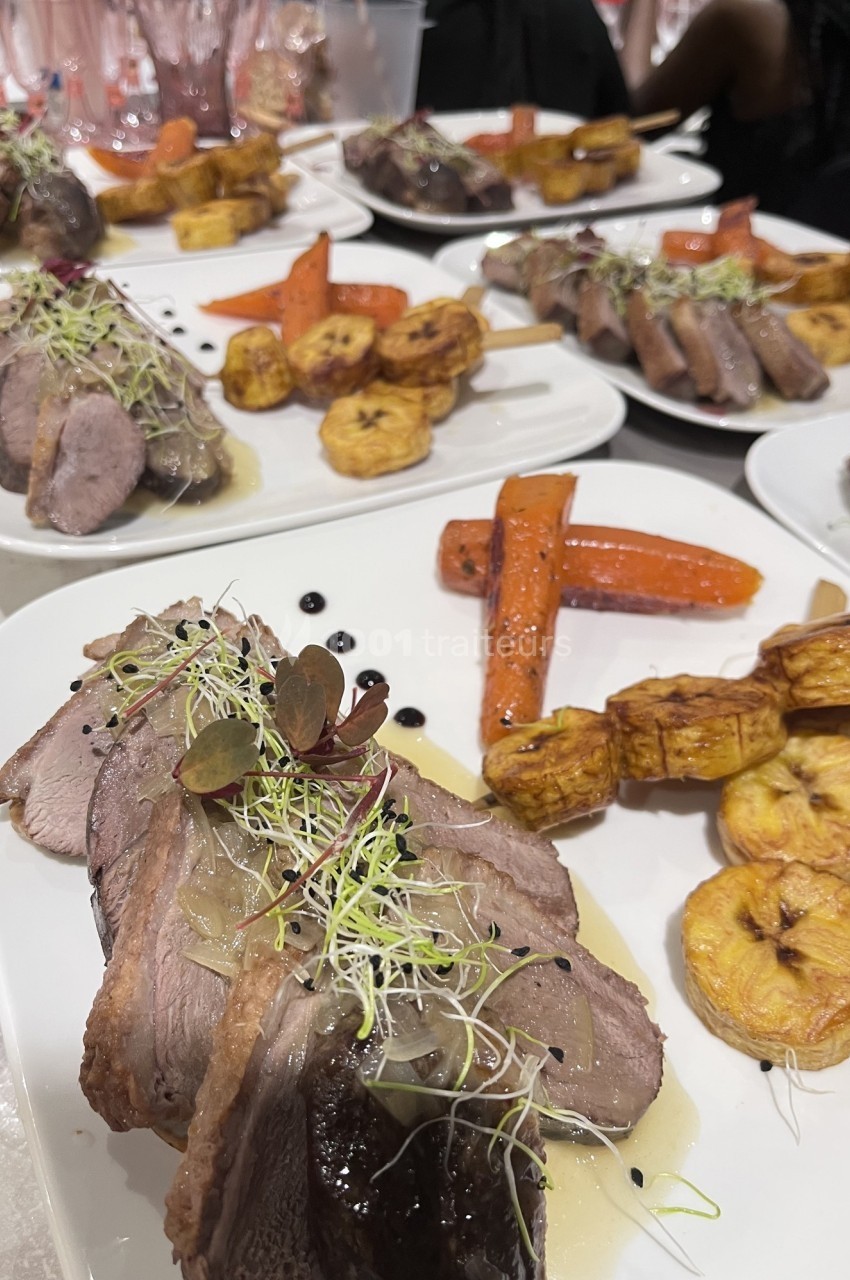 Assiettes de viande tranchée avec sauce, accompagnées de bananes plantains, carottes rôties et germes décoratifs.