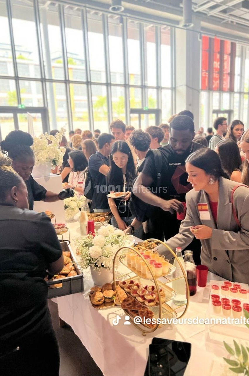 Des personnes se servent à un buffet garni de plats variés dans un espace lumineux avec de grandes fenêtres.