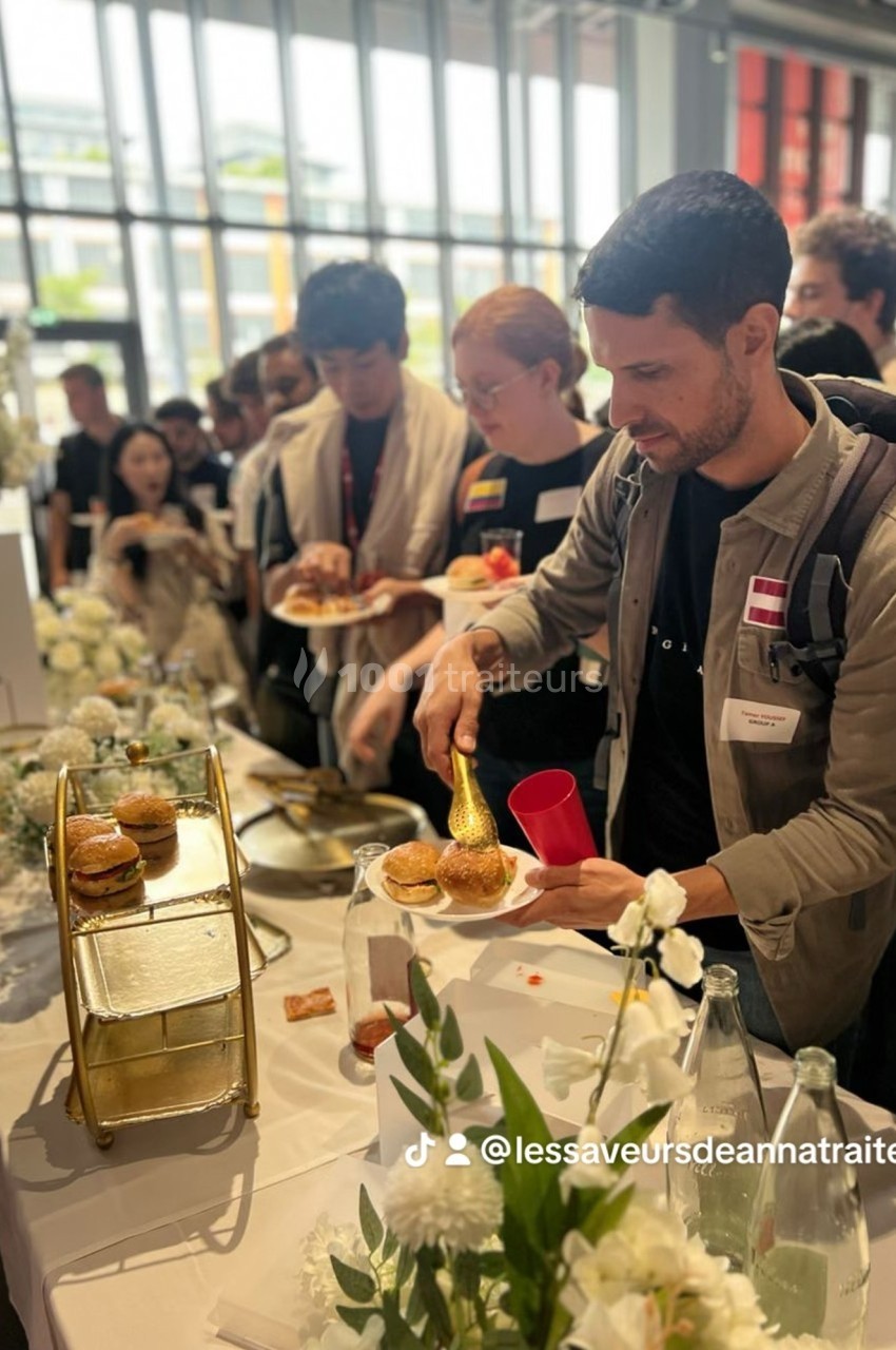Des personnes se servent à un buffet avec des fleurs blanches en décoration dans un espace lumineux.