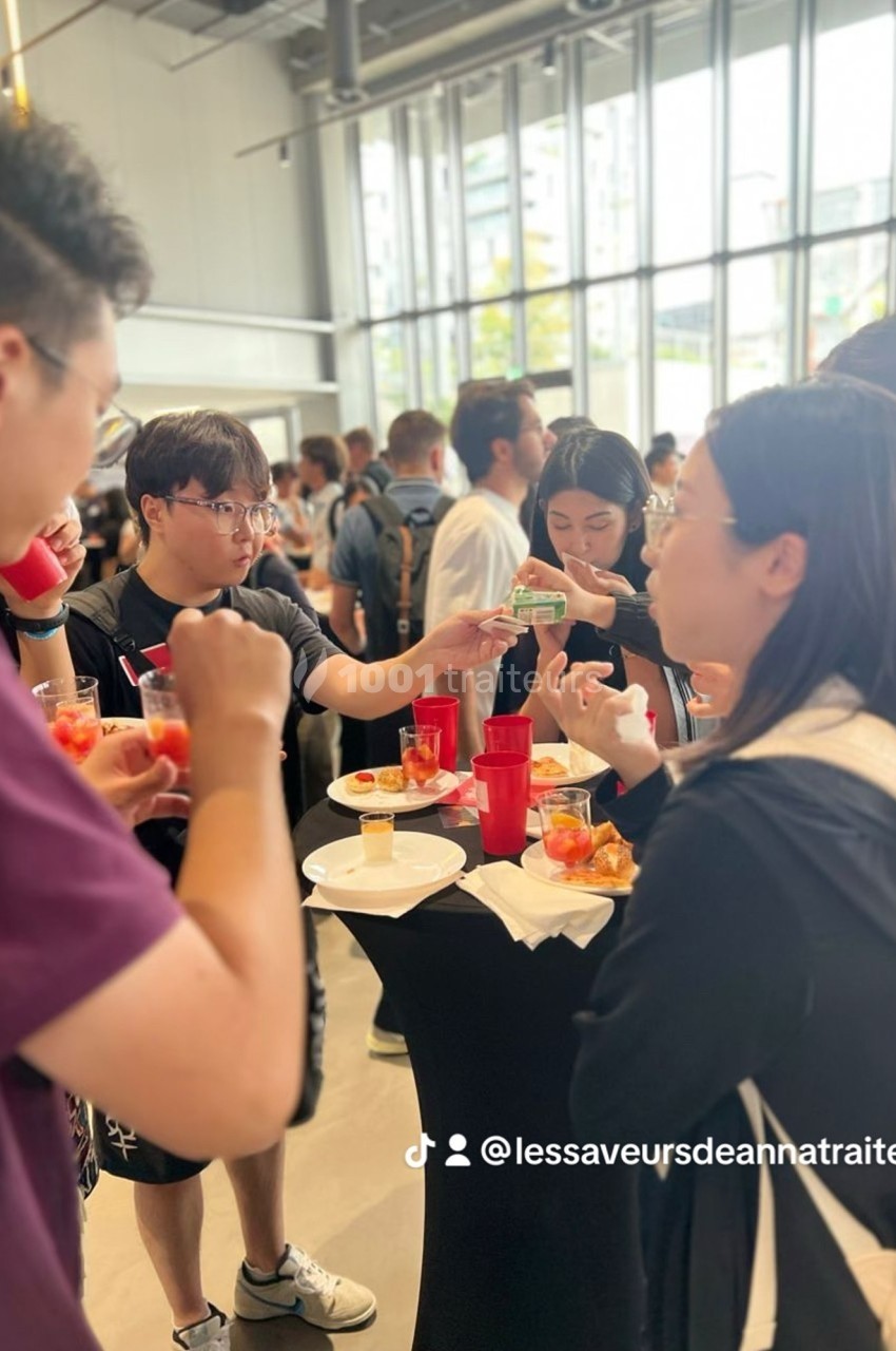 Des personnes debout autour de tables hautes dégustent des amuse-bouches et discutent dans un espace lumineux.