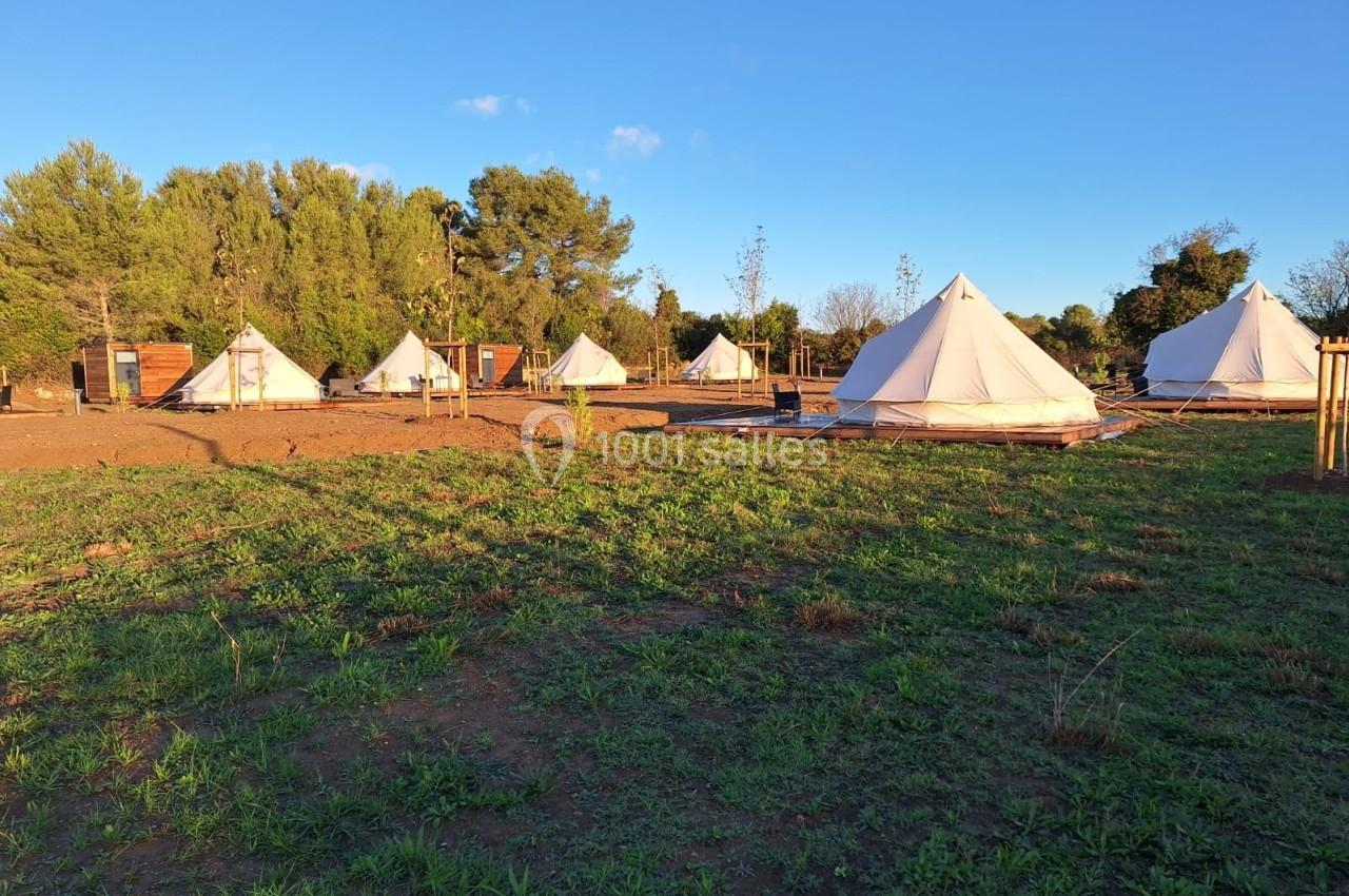 Des tentes blanches installées sur un terrain herbeux, entourées d'arbres sous un ciel dégagé en fin de journée.