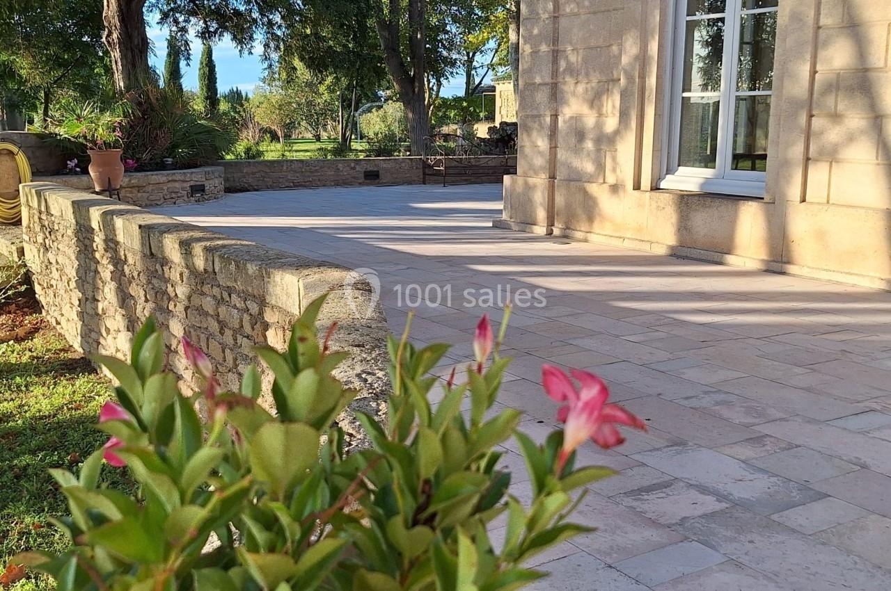 Terrasse en pierre bordée d'un muret en pierre, avec des plantes et des arbres en arrière-plan.