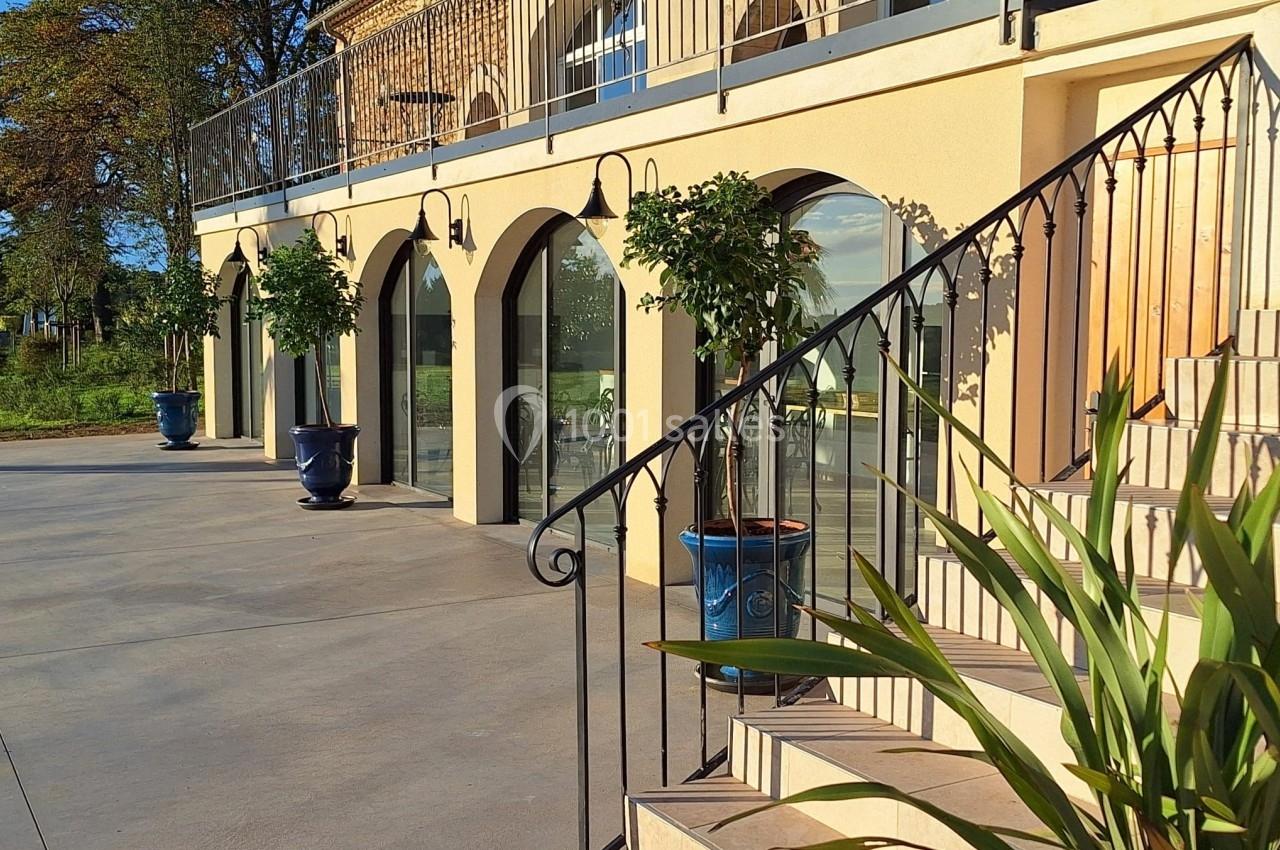 Façade ensoleillée d'un bâtiment avec arches vitrées, pots de fleurs bleus et escalier en premier plan.