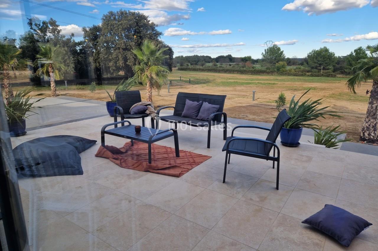 Mobilier de jardin noir avec coussins et tapis sur une terrasse en pierre, vue sur un paysage arboré et dégagé.