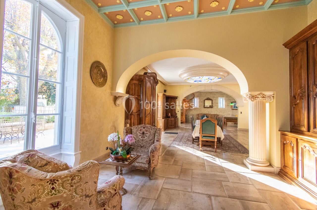 Salle à manger lumineuse avec mobilier en bois, voûtes, colonnes décoratives et vue sur un jardin par une grande fenêtre.