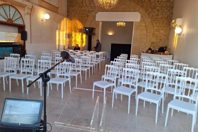 Salle de conférence lumineuse avec rangées de chaises blanches, un pupitre et un micro au premier plan.