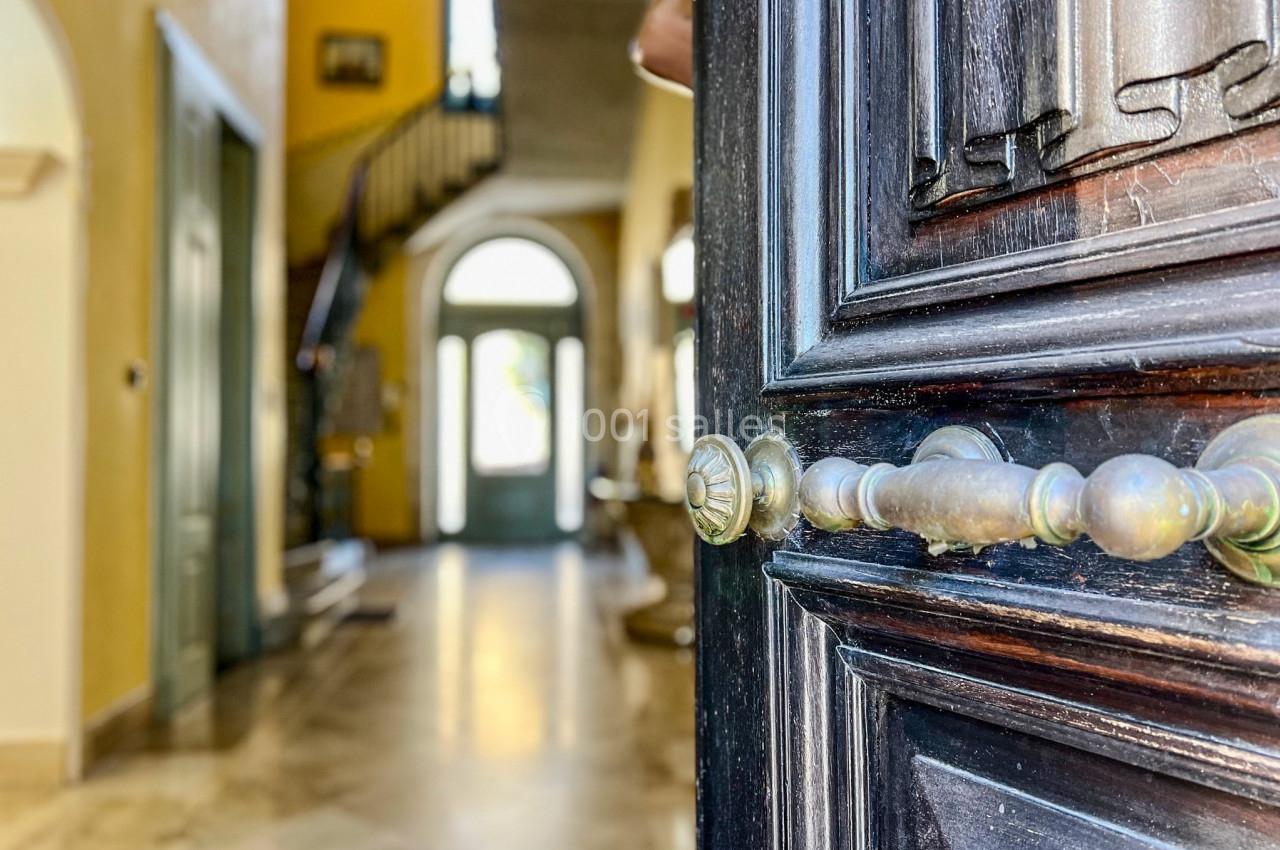 Porte en bois sombre entrouverte donnant sur un hall d'entrée lumineux avec escalier et sol en marbre.