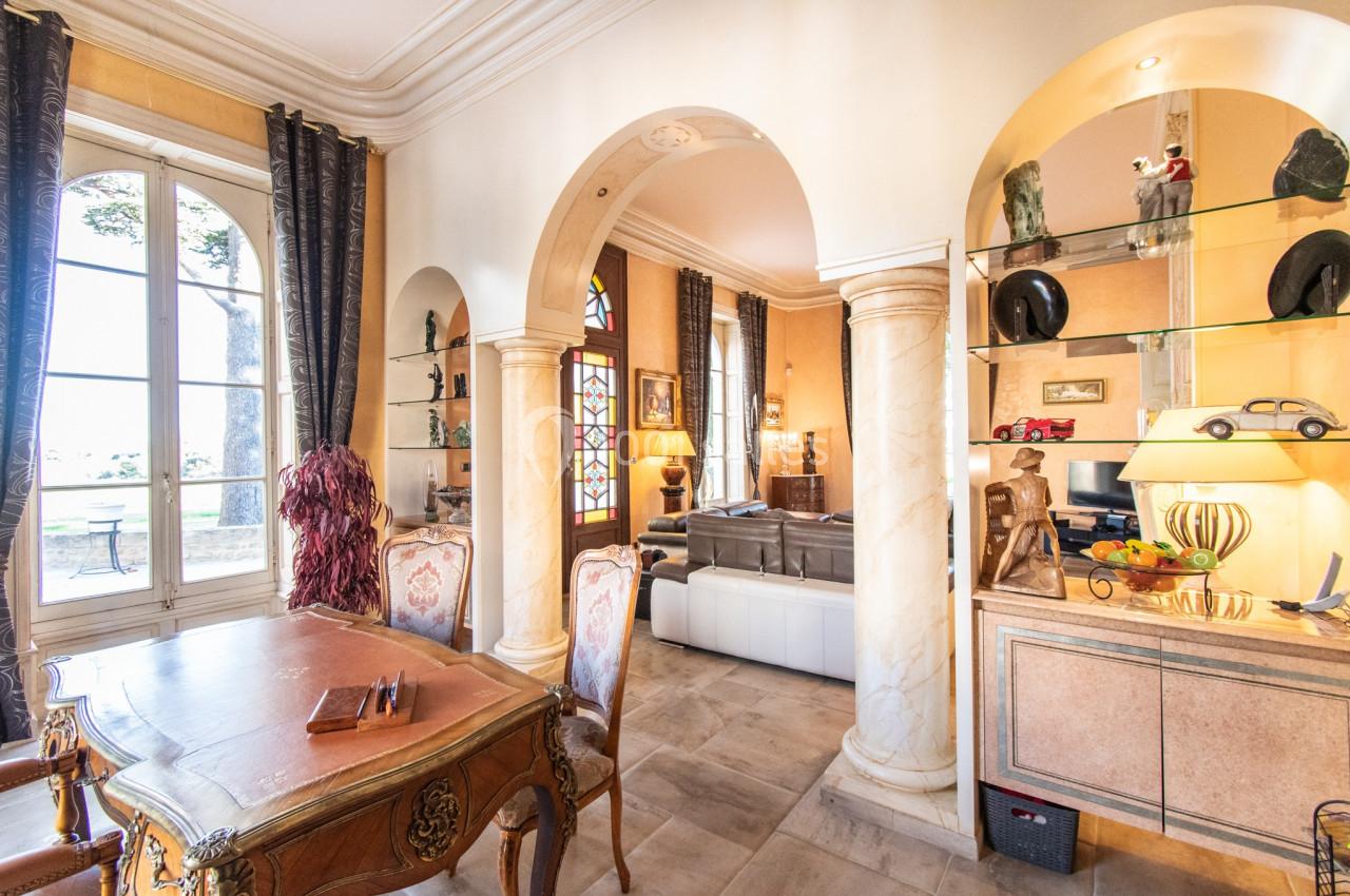 Salle de séjour lumineuse avec arches, mobilier classique, étagères décoratives et vue sur un jardin à travers une grande…