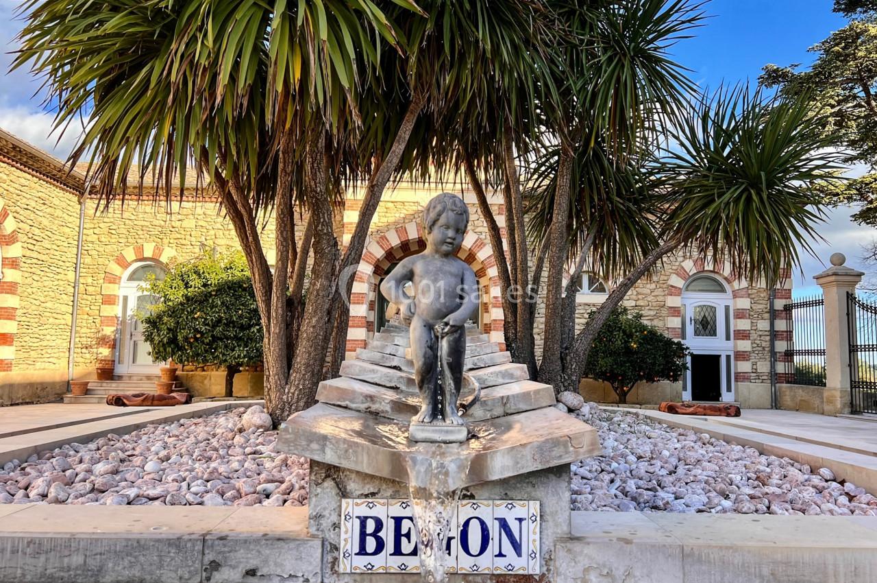 Statue d'enfant ornant une fontaine devant un bâtiment en pierre avec des palmiers et des galets décoratifs.