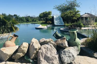 Vue d'un bassin avec toboggans aquatiques, entouré de végétation, de rochers et de jarres décoratives.