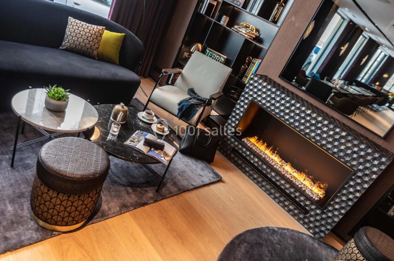 Salon moderne avec canapé, fauteuil, table basse, cheminée électrique allumée et décoration contemporaine.