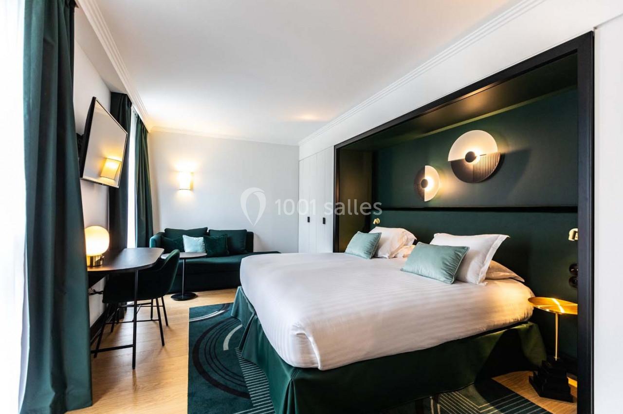 Chambre moderne avec lit double, canapé, bureau, éclairage design et décoration aux tons verts et blancs.