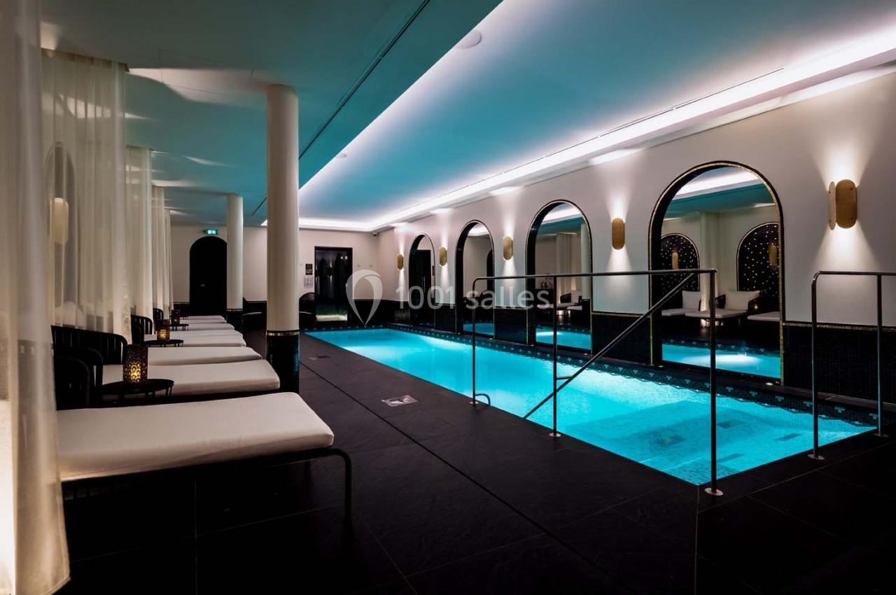 Piscine intérieure éclairée avec des chaises longues alignées et des arches décoratives sur les murs.