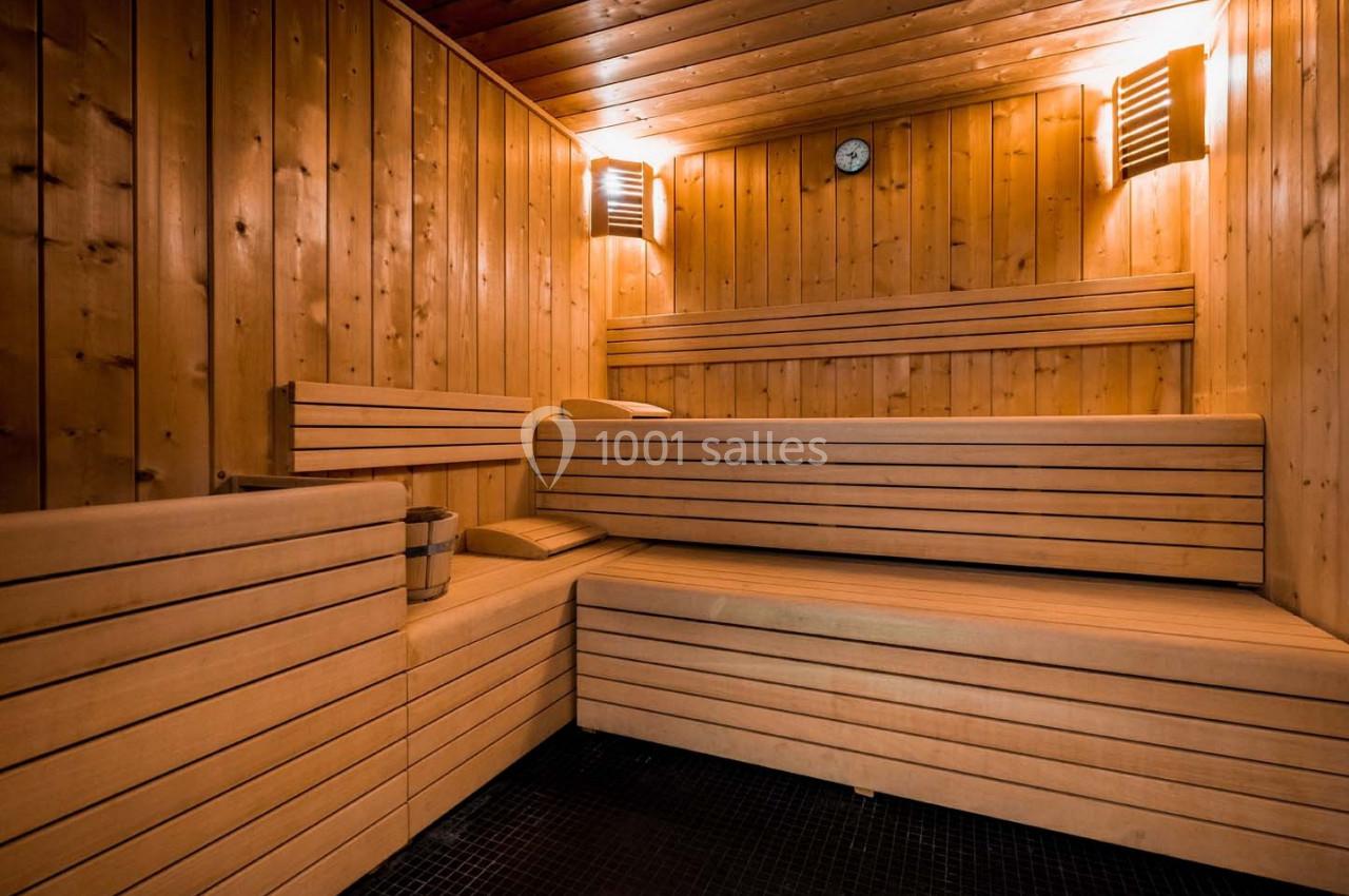 Intérieur d'un sauna en bois avec bancs en gradins, seau en métal et lumière tamisée.