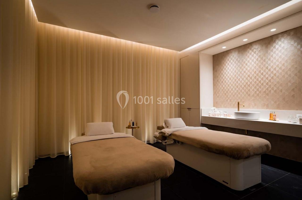 Salle de soins avec deux tables de massage, éclairage tamisé et décor minimaliste dans des tons neutres.
