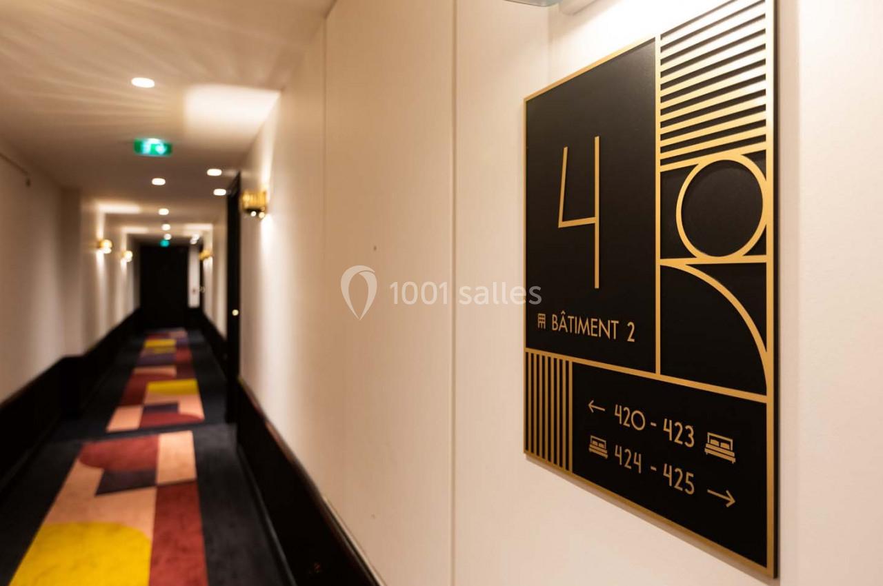 Panneau indiquant le numéro 4, bâtiment 2, avec des flèches vers les chambres 420-423 et 424-425 dans un couloir d'hôtel.