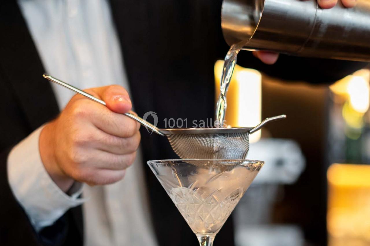 Un barman verse un cocktail filtré dans un verre à martini rempli de glace.