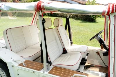 Vue latérale intérieure d'une voiture décapotable vintage avec sièges blancs bordés de rouge et toit en toile.