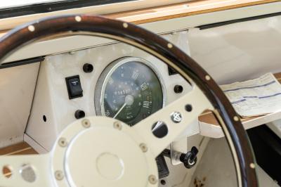 Vue latérale intérieure d'une voiture décapotable vintage avec sièges blancs bordés de rouge et toit en toile.