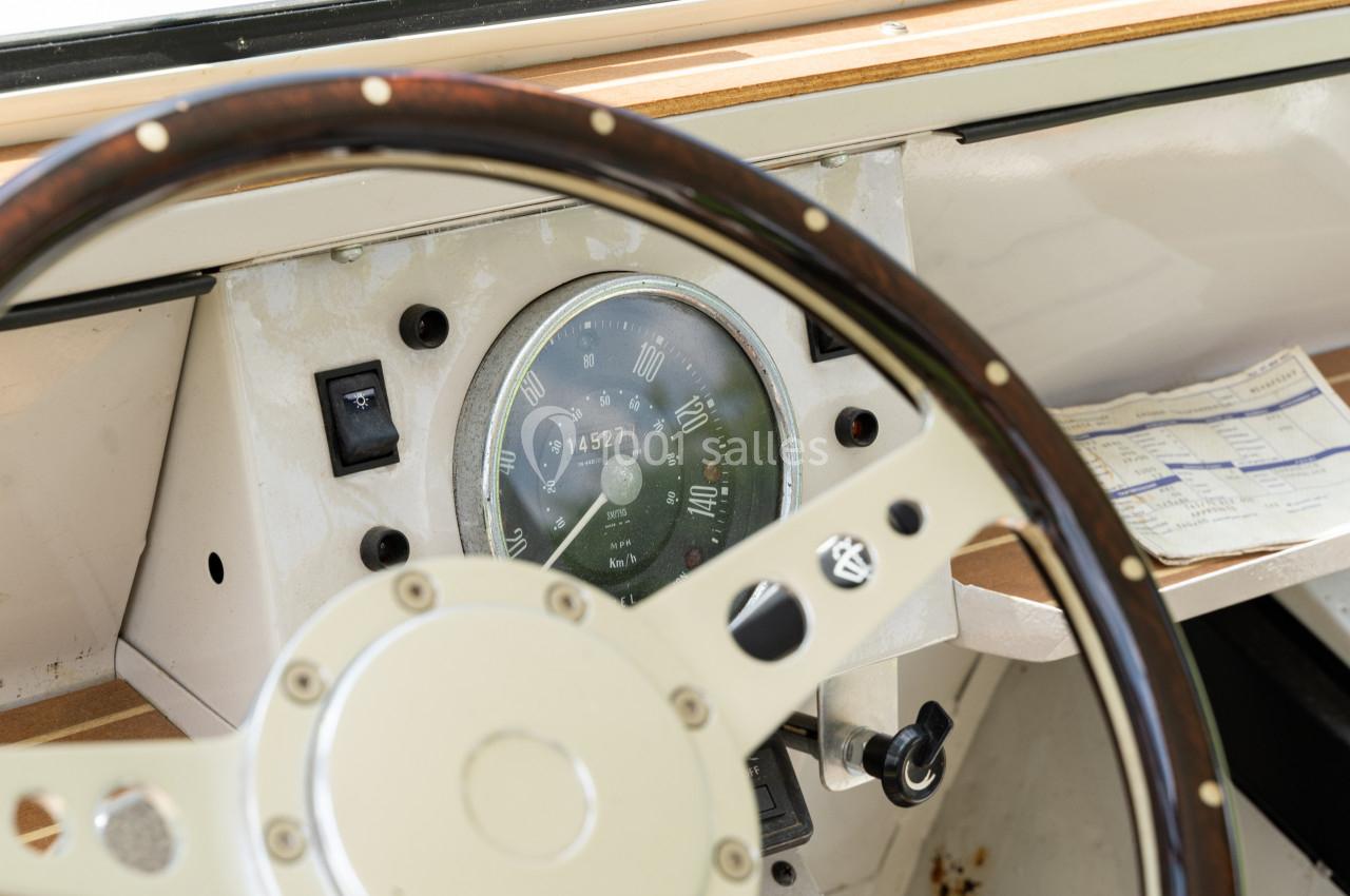Volant en bois et tableau de bord d'un bateau avec un compteur et un document posé à côté.