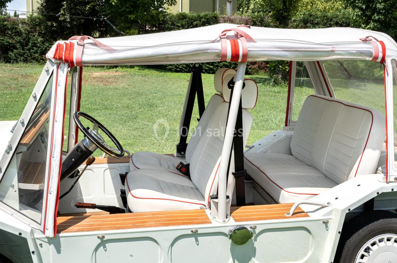 Vue latérale intérieure d'une voiture décapotable vintage avec sièges blancs bordés de rouge et toit en toile.