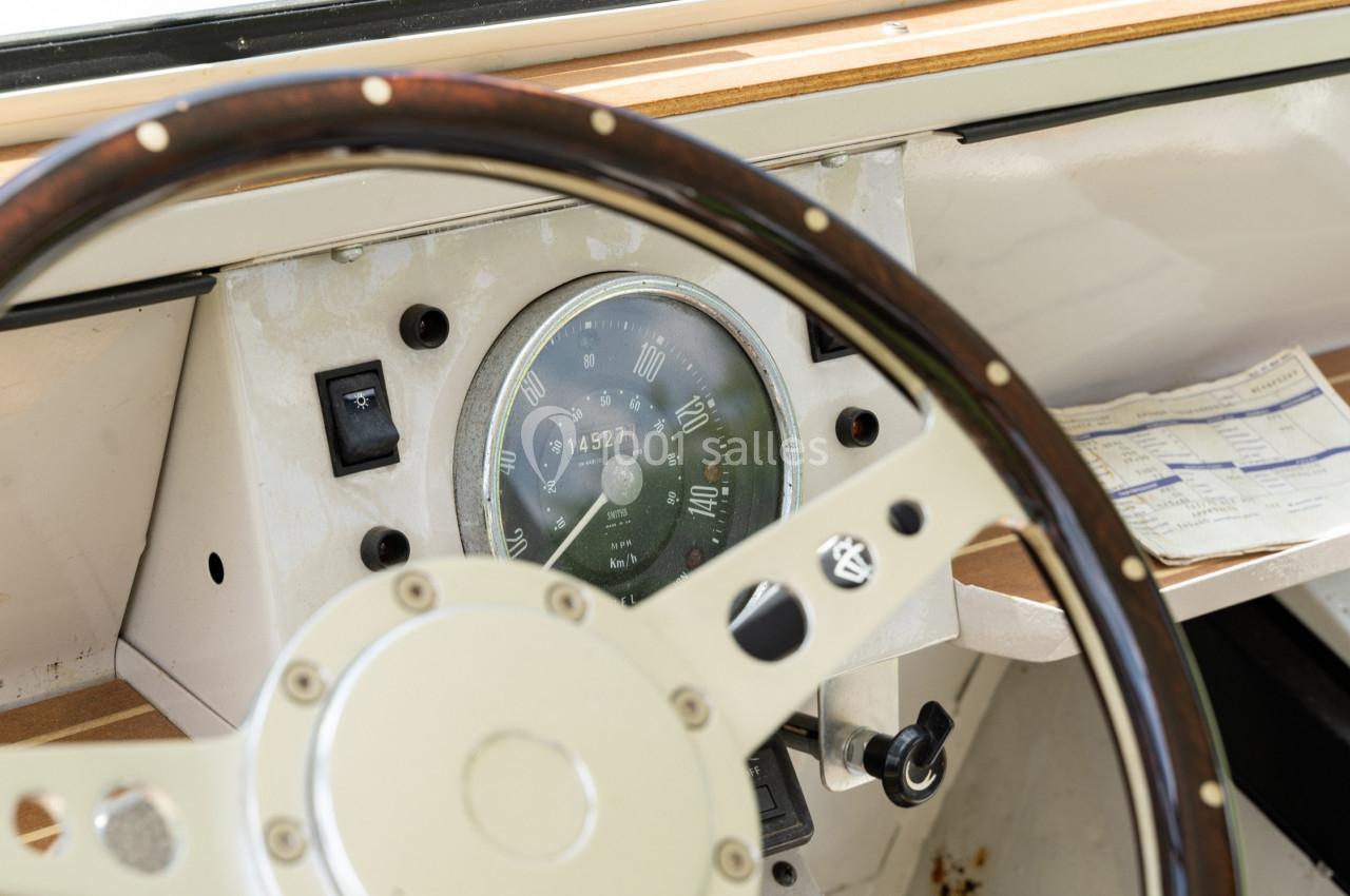 Volant en bois et tableau de bord d'un bateau avec un compteur de vitesse et un document posé à côté.