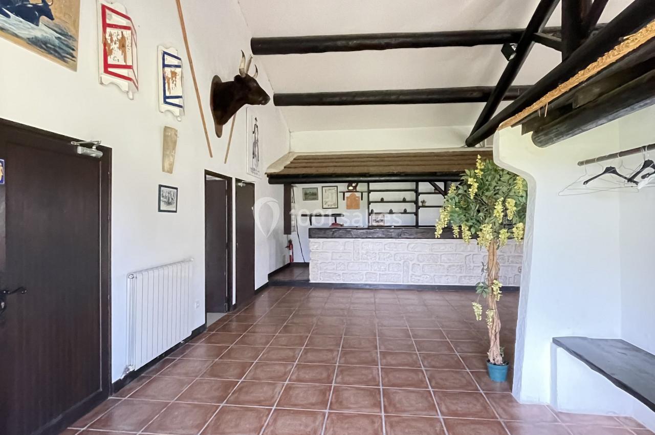 Hall d'entrée avec comptoir d'accueil, plafond en poutres apparentes, murs décorés et sol en carrelage.