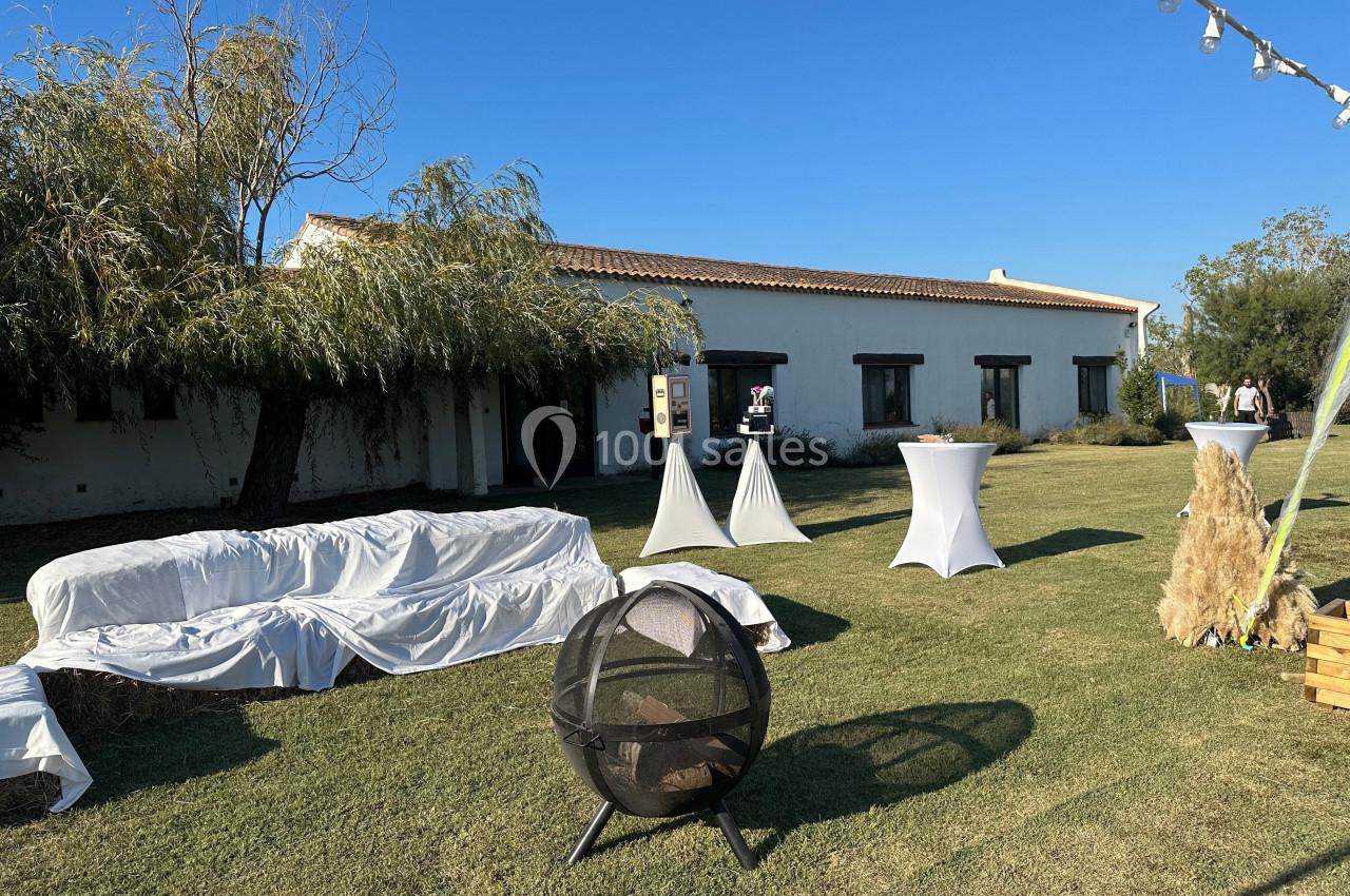 Espace extérieur avec pelouse, mobilier de réception, bâtiment blanc en arrière-plan et ciel dégagé.