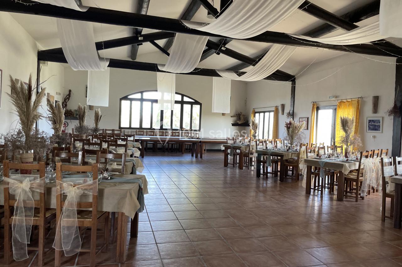Salle de réception décorée avec des tables dressées, des chaises ornées de nœuds et des éléments végétaux.