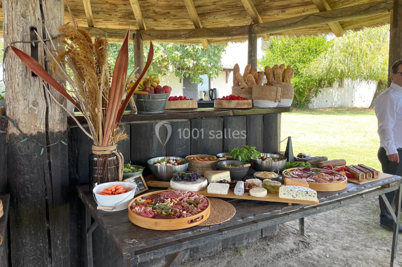 Buffet rustique en extérieur avec charcuterie, fromages, pains, légumes frais et fruits disposés sur une table en bois.