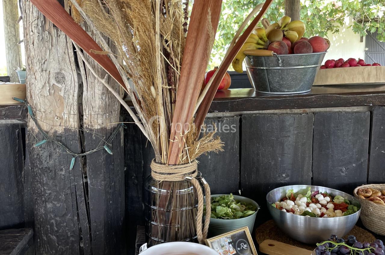 Plateau de charcuterie et légumes frais sur une table en bois, avec des fruits et une décoration végétale en arrière-plan.