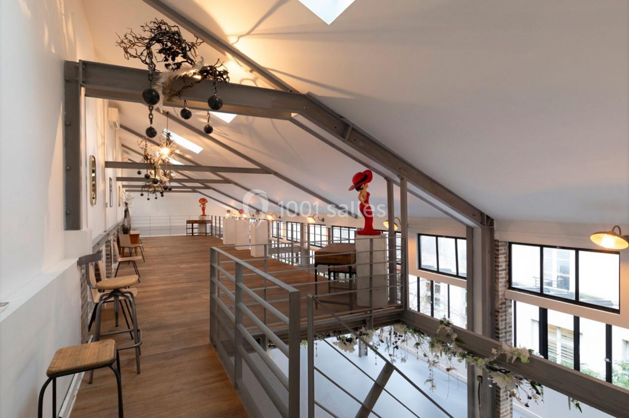 Intérieur d'un loft avec mezzanine, poutres apparentes, grandes fenêtres et décoration moderne.