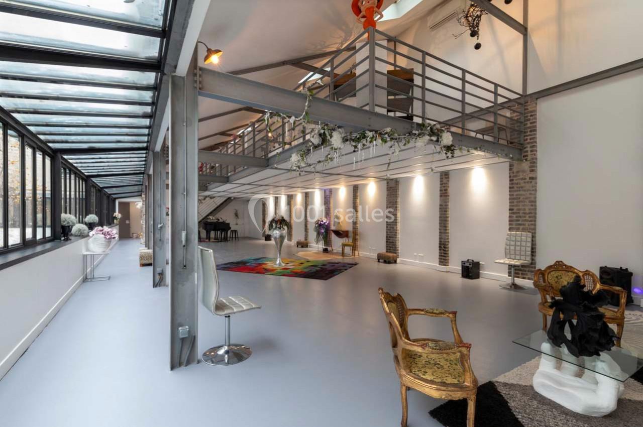 Intérieur spacieux et lumineux d'un loft avec mezzanine, murs en briques, verrière et mobilier éclectique.