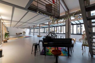 Escalier en bois à côté d'une composition florale blanche, avec un piano et un tapis coloré en arrière-plan.