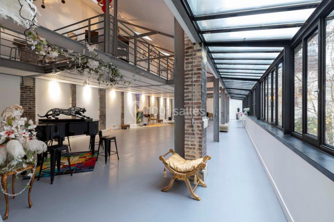 Intérieur spacieux et lumineux avec mezzanine, grandes baies vitrées, piano noir et décorations florales.