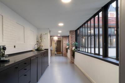 Escalier en bois à côté d'une composition florale blanche, avec un piano et un tapis coloré en arrière-plan.