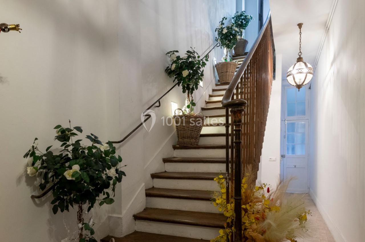Escalier en bois avec rampe métallique, décoré de plantes en pots et éclairé par une suspension lumineuse.