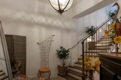 Escalier en bois à côté d'une composition florale blanche, avec un piano et un tapis coloré en arrière-plan.