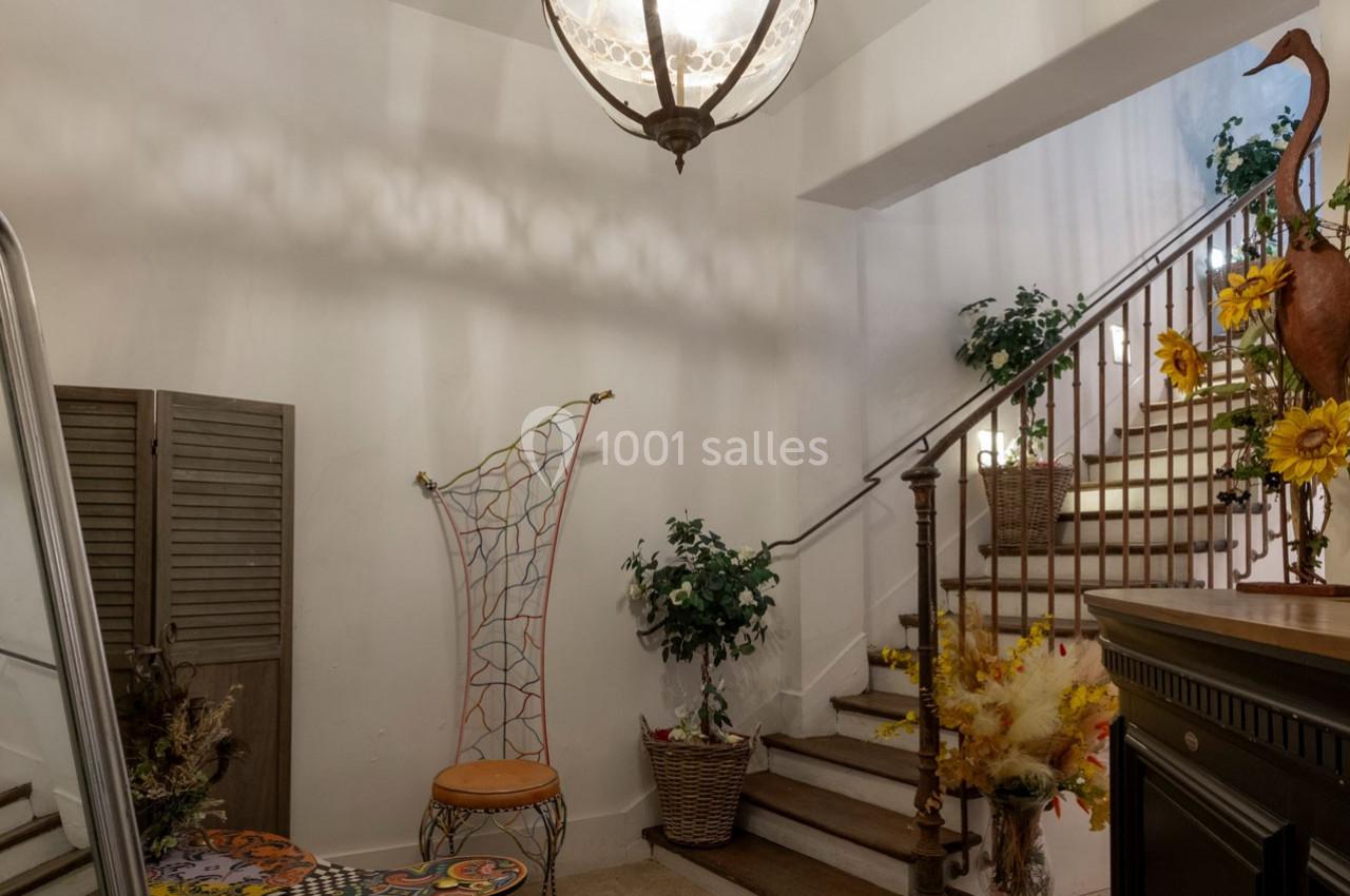 Escalier intérieur décoré avec des plantes, des fleurs et une chaise artistique dans un coin lumineux.
